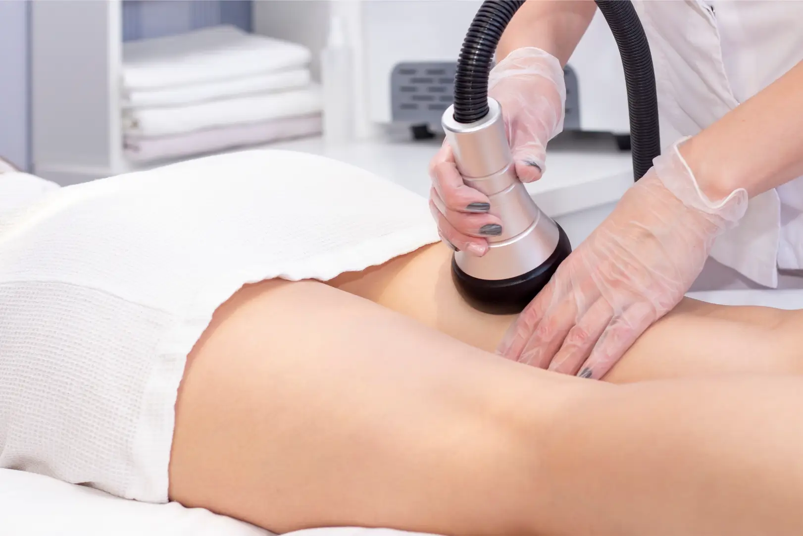 Practitioner wearing transparent gloves applies a handheld treatment device to a person's upper thigh near the hip.
