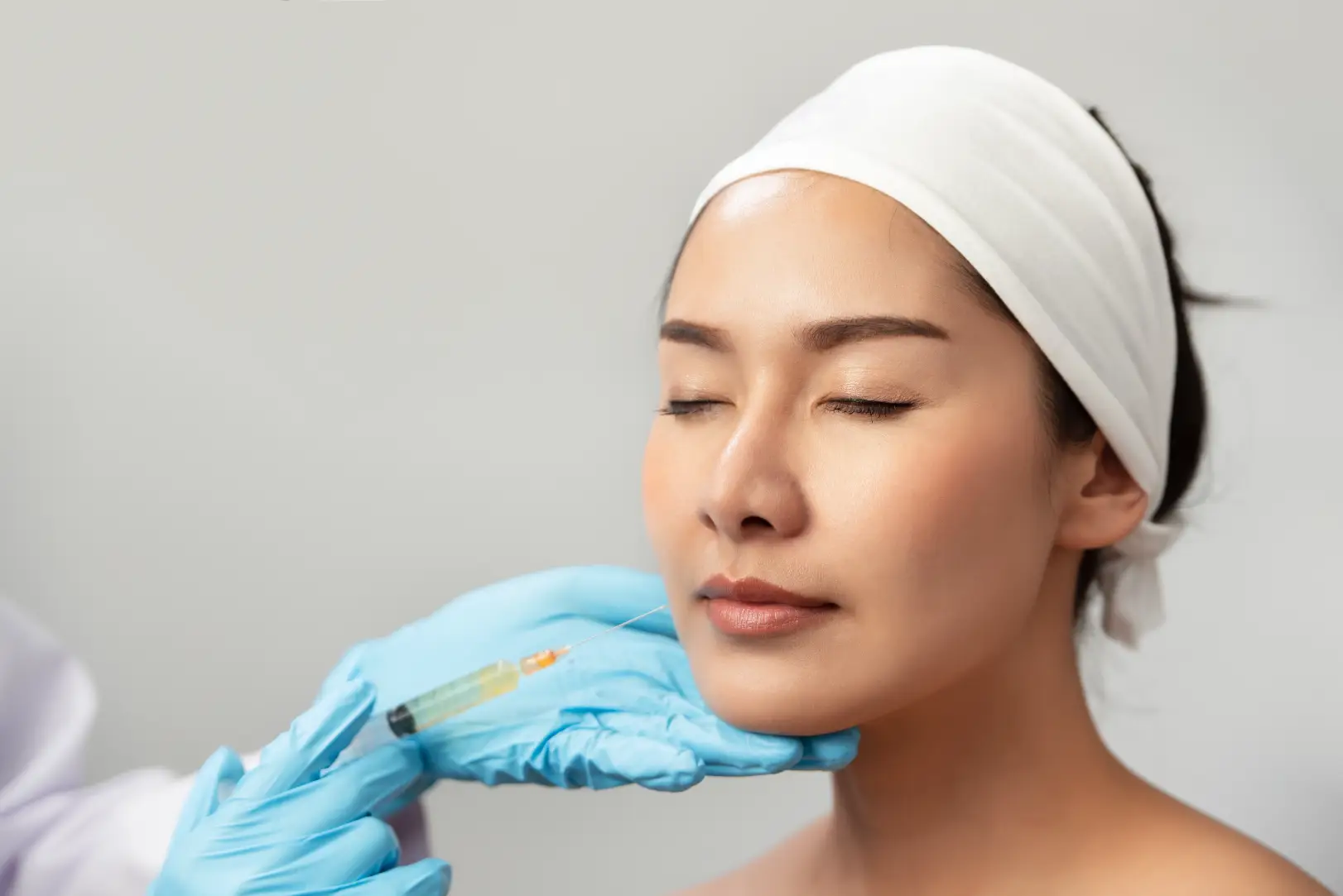 Woman with eyes closed while a clinician holds a syringe near her lower cheek and chin.